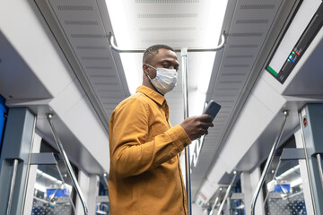 Naklejka na ściany i meble A businessman in a protective mask with a mobile phone rides in a subway car to the office