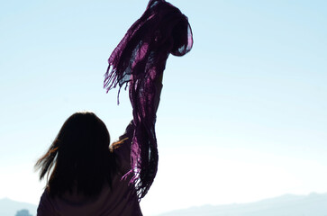 Woman raising a lilac feminist scarf in protest against gender violence. Free blue background. Focus on the lilac scarf - obrazy, fototapety, plakaty