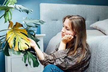 Fototapeta Young upset, sad woman examining dried dead foliage of her home Monstera plant. Houseplants diseases. Diseases Disorders Identification and Treatment, Houseplants sun burn. Damaged Leaves obraz