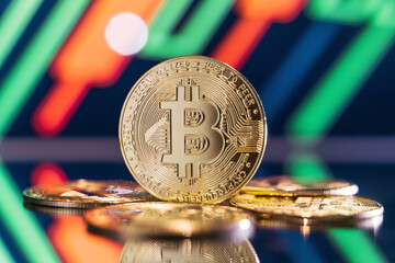 Golden bitcoin standing on mirror surface reflecting blurred background with crypto chart with green and red candlesticks. Cryptocurrency trading market concept