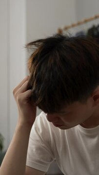 Vertical Screen: closeup shot of a tired asian male rubbing his temples with a painful look for he is having bad headache from hangover after waking up in the morning at home.