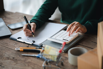 Person pressing white calculator, online store owner checking product order before shipping to customer, selling product through online channels on website and product platform.