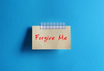 Old note paper stick on blue background with note written FORGIVE ME, to ask someone to forgive,...