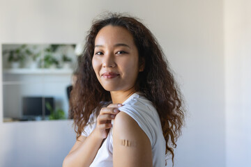 Young Asian woman with adhesive bandage on her arm after Corona virus vaccine. First aid. Medical,...