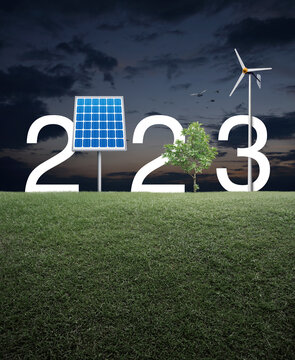 2023 white text with solar cell, wind turbine and growing tree on green grass field over sunset sky, Happy new year 2023 ecological cover concept