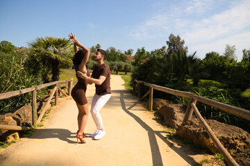 Obraz premium Handsome young man and woman dancing bachata and salsa in the park. The couple dance passionately surrounded by greenery. Dancing concept.