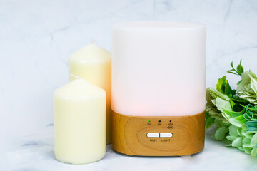 Aroma composition with a modern aroma oil diffuser light on seven chakras on marble surface with white candles and flowers, Aromatherapy at home. Mindfulness lifestyle. Close up view with copy space