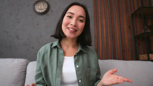 Web cam view head shot close up young woman of Asian ethnicity in casual clothe record video call talk use pc laptop sits on sofa stay home flat rest relax spend free spare time in living room indoor