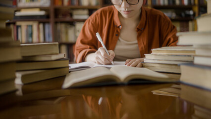 Female student in eyeglasses taking notes, studying books in college library