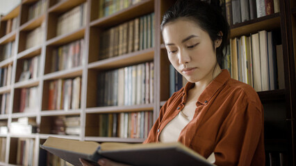Young asian woman student reading a book in university library, doing research