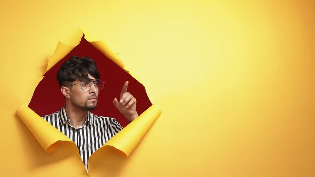 Solution discovery. Useful information. Dilemma contemplation. Pensive puzzled man considering pros and cons in orange breakthrough torn paper hole on copy space background.
