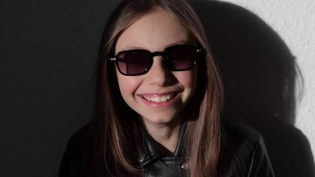 Slow motion video of a stylish child in leather jacke with glasses , the wind blows in her face and inflates the hair
