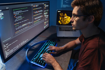 Profile view of young developer programming at home office, man in shirt and glasses writing code...