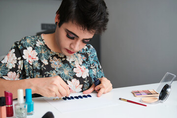 Young transgender man in a dress painting false nails.