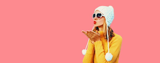 Winter portrait of young woman blowing her red lips sending air kiss wearing colorful knitted...