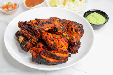 Tandoori chicken is a popular roast chicken recipe from India. Tandoor is a traditional wood oven. Chicken Tandoori Platter is served in a white plate with salad and chutney. Copy Space.