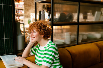 Mid white woman with curly hair reading book while sitting in cafe