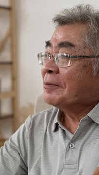 Vertical Screen: tired senior man yawning while relaxing on sofa indoors. sleepy aged male sitting on couch. old grandpa cover mouth with hand resting in living room