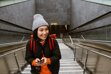 Beautiful smiling asian woman using smartphone while climbing the stairs