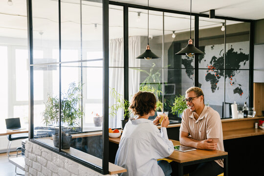 Two Smiling Colleagues Talking During Coffee Break In Office Kitchen