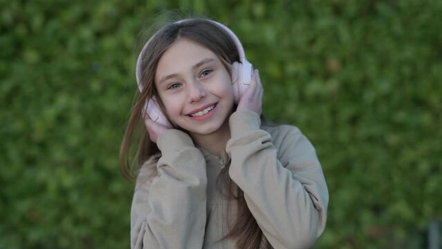 Smiling child listening to music outdoors, smiling little girl in headphones has a fun with music