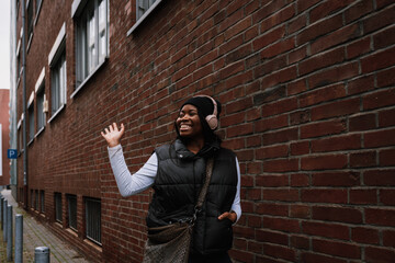 Cheerful afro woman waving hand while walking outdoors