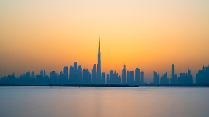 A stunning view of the Dubai skyline at sunset, as seen from the water. The golden light reflects on the skyscrapers and the Burj Khalifa, the world's tallest building. 