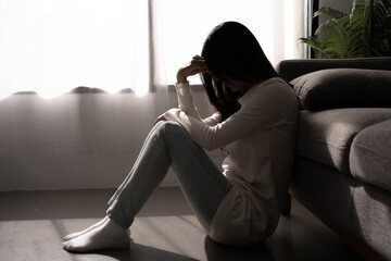 Young woman feeling depressed and stressed sitting in dark bedroom. Mental Health Concept.