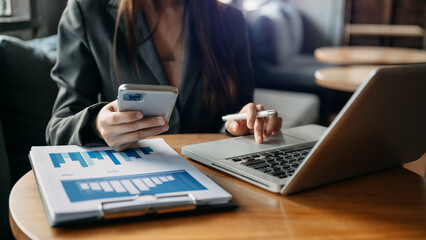 business documents on office table with smart phone and digital tablet and graph financial and woman working at office