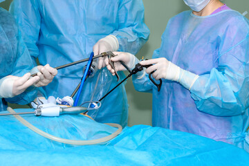 Hands of surgeons in sterile gloves use laparoscopic surgical instruments. A team of surgeons...