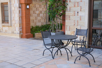 Elegant metal black chairs and table in a cafe on the street against of the buildings with stone brick wall in the town