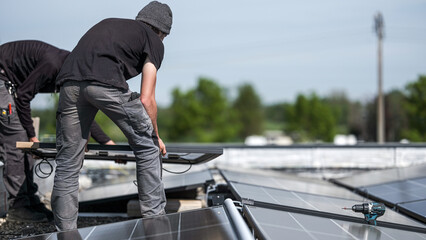 Male team engineers installing stand-alone solar photovoltaic panel system. Electricians mounting blue solar module on roof of company roof. Alternative energy concept