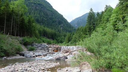 Fototapeta na wymiar Flusslauf mit kleinem Wasserfall in den Bergen von Italien im Norden
