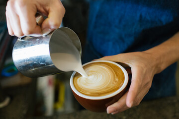 Close up shot of a man's holding a cup of coffee also pouring milk in a tin mug to the coffee
