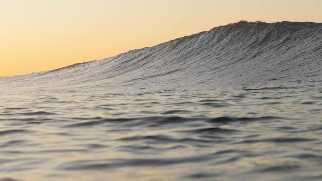 A beautiful wave breaks as the sun rises in the background. The water is backlit in the early morning light.