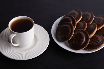 A photo of a lot of chocolate chip cookies on a plate with a cup of drink next to it