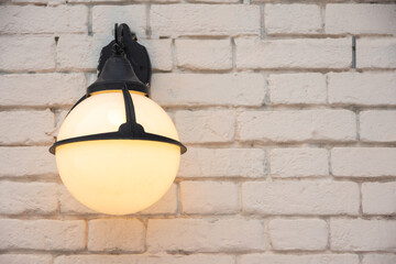 A burning round antique lantern on a light brick wall, copy space. circle glass wall lamp on white wall.
