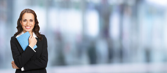 Portrait image of happy smiling business woman black confident suit with notepad organizer. Executive office worker, teacher or real estate agent,  over blurred office background