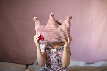 Happy kid girl with soft crown shaped pillow. Princess girl. Pink.
