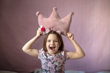 Happy kid girl with soft crown shaped pillow. Princess girl. Pink.