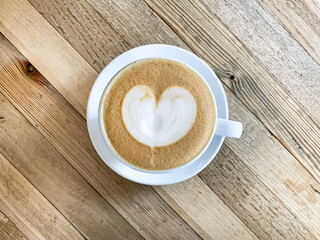A cup of coffee latte on a wooden table. A mug of flat white coffee, latte, cappuccino on a wooden background. Coffee art. Heart flower shape latte art