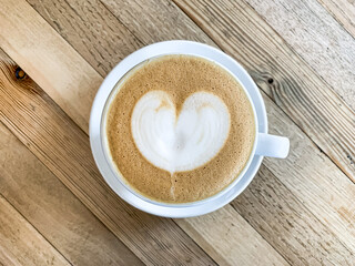 A cup of coffee latte on a wooden table. A mug of flat white coffee, latte, cappuccino on a wooden background. Coffee art. Heart flower shape latte art