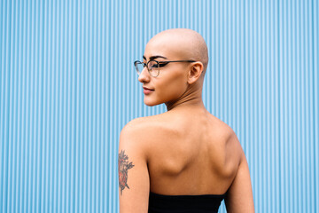 Woman with shaved head in front of blue wall