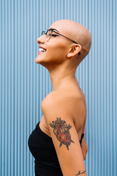 Happy woman with shaved head by blue wall