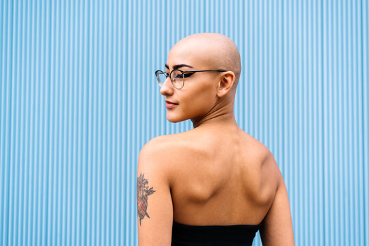 Woman with shaved head in front of blue wall