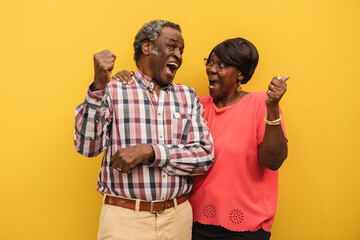 Excited senior couple cheering against yellow background