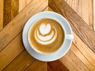 A cup of coffee latte on a wooden table. A mug of flat white coffee, latte, cappuccino on a wooden background. Coffee art. Heart flower shape latte art