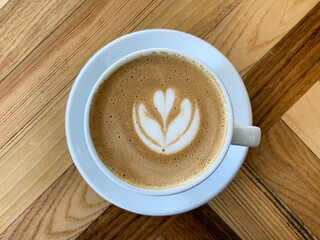 A cup of coffee latte on a wooden table. A mug of flat white coffee, latte, cappuccino on a wooden background. Coffee art. Heart flower shape latte art