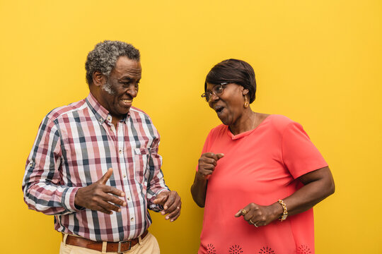 Happy senior couple dancing against yellow background