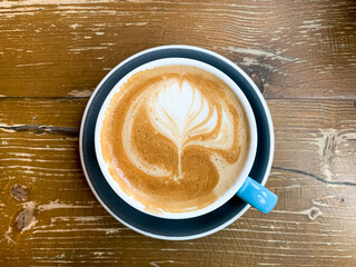 A cup of coffee latte on a wooden table. A mug of flat white coffee, latte, cappuccino on a wooden background. Coffee art. Heart flower shape latte art